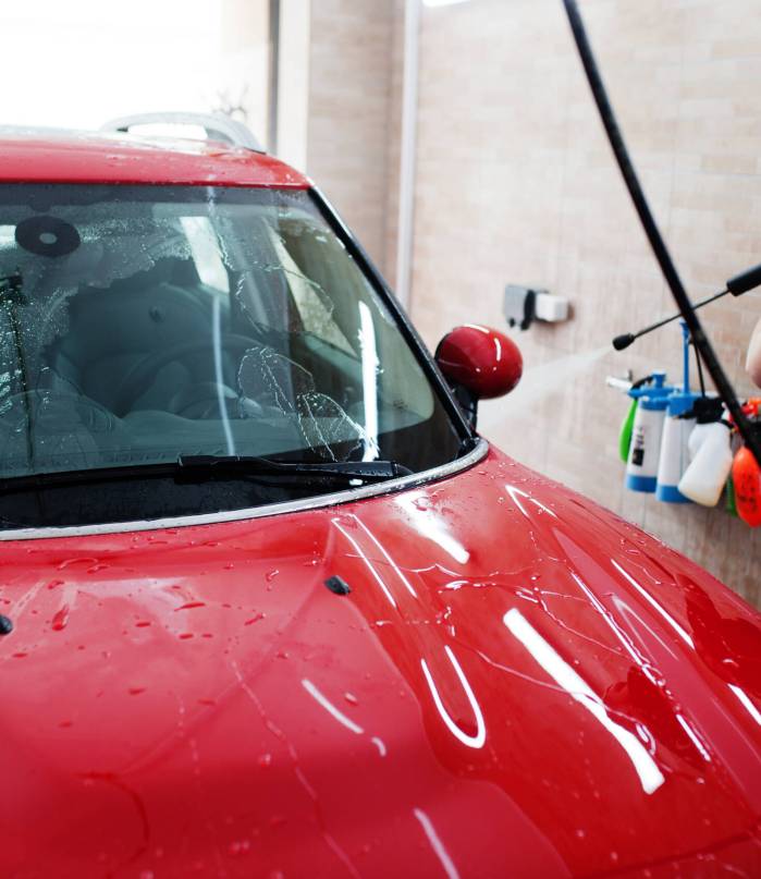 Man worker washing red car in detailing garage. Man worker washing red car in detailing garage.